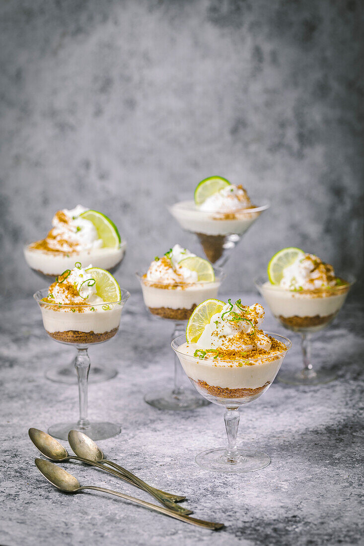 Arrangement of lime parfaits and biscuit crumbs in vintage cocktail glasses with lime garnish on a grey background