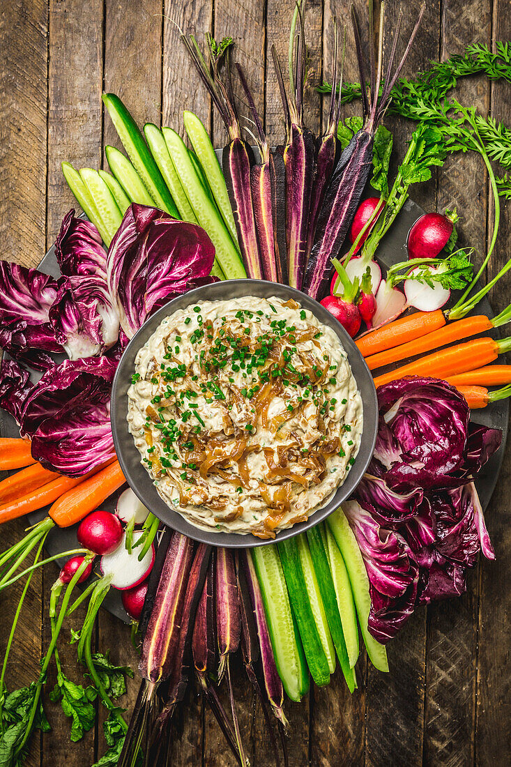 Close, overhead shot of onion dip in a bowl surrounded by fresh, colorful vegetables on a wood background