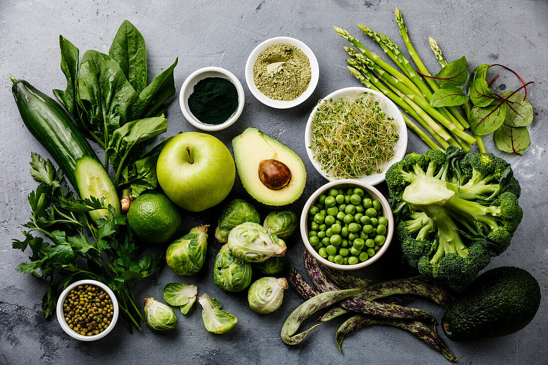 Gesundes Grünes Essen Sauberes Essen Auswahl Proteinquelle für Vegetarier: Avocado, Spargel, Apfel, Brokkoli, Spinat, Spirulina, grüne Erbsen auf grauem Betonhintergrund