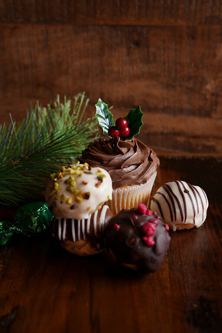 Weihnachtlicher Schokoladen-Cupcake und Profiteroles vor einem dunklen Holzhintergrund, mit Kopierbereich