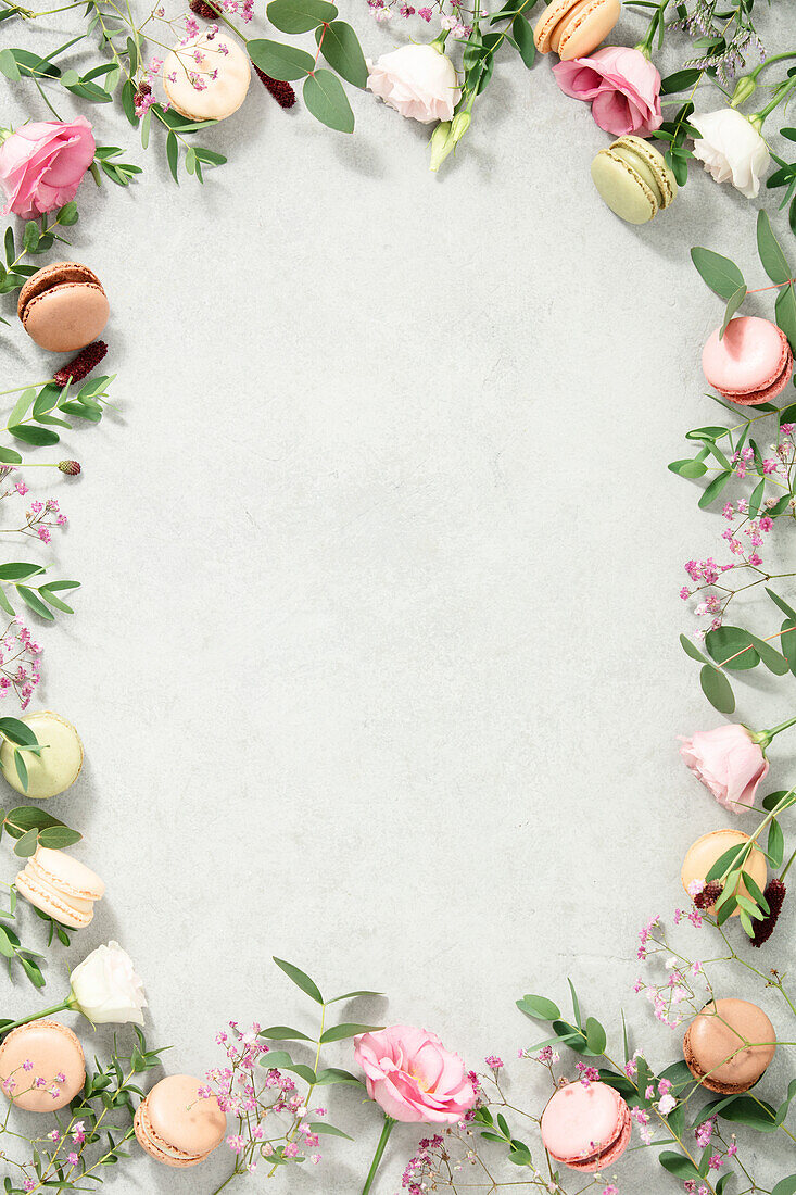 Frame of spring flowers and various types of macaroons laid flat