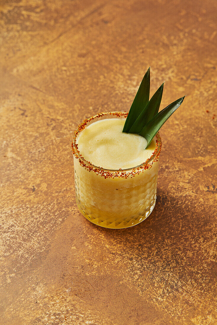 Pineapple mocktail with leaf garnish on a gold background