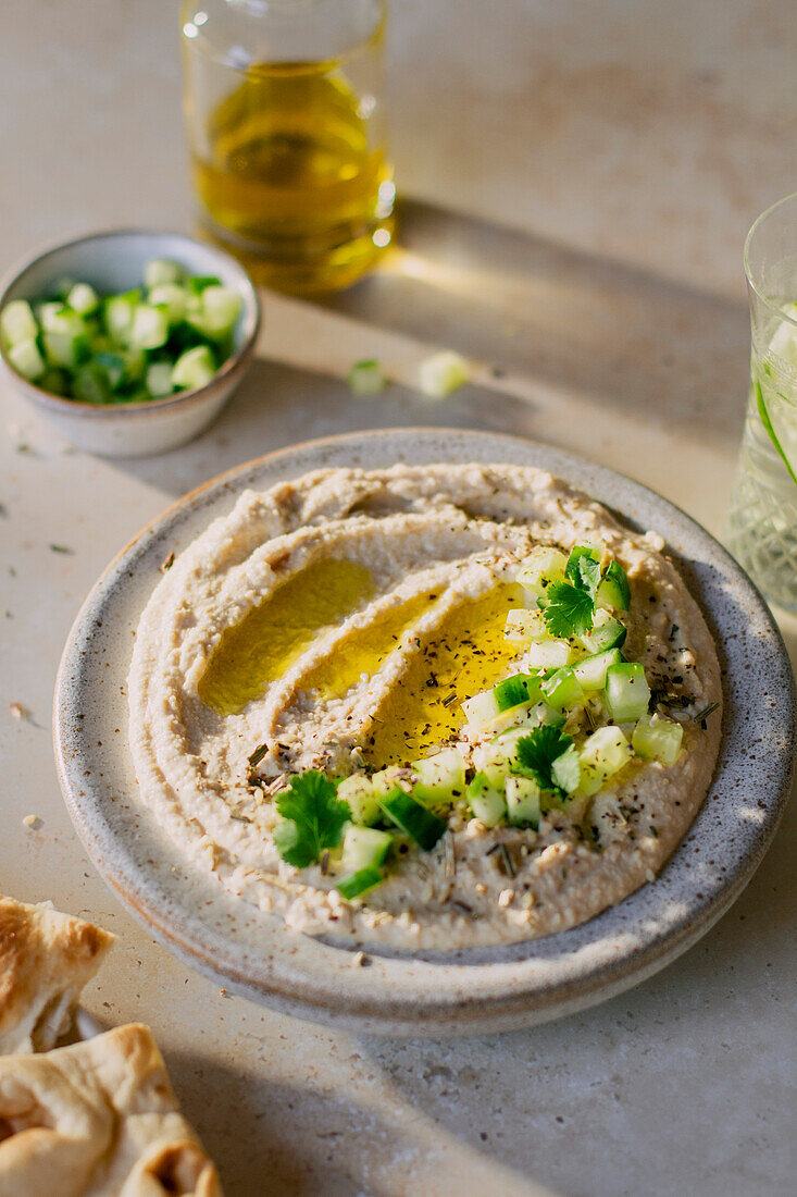 Creamy hummus dip with cucumber and olive oil pour in hard light