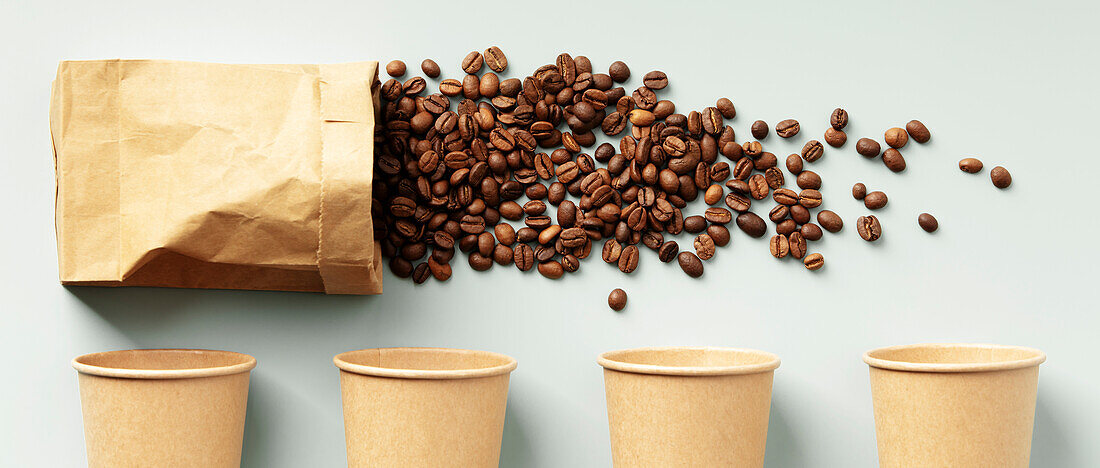 A scattering of coffee beans around plain paper cups on a table