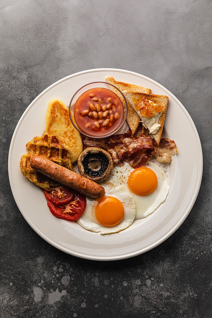 Full fry up English breakfast with fried eggs, sausages, bacon, beans, toasts