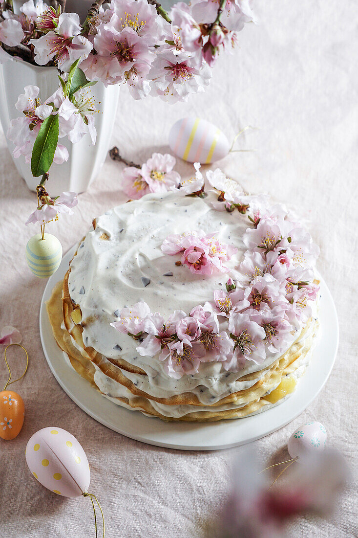 Crepe cake or blini cake for Easter, pink background, almond blossoms, pink background, women's hands