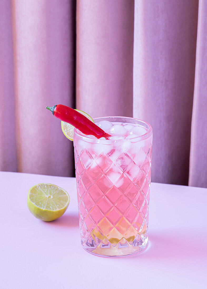 Clear glass filled with refreshing cold cocktail with pepper and ice cubes served on the table with lime