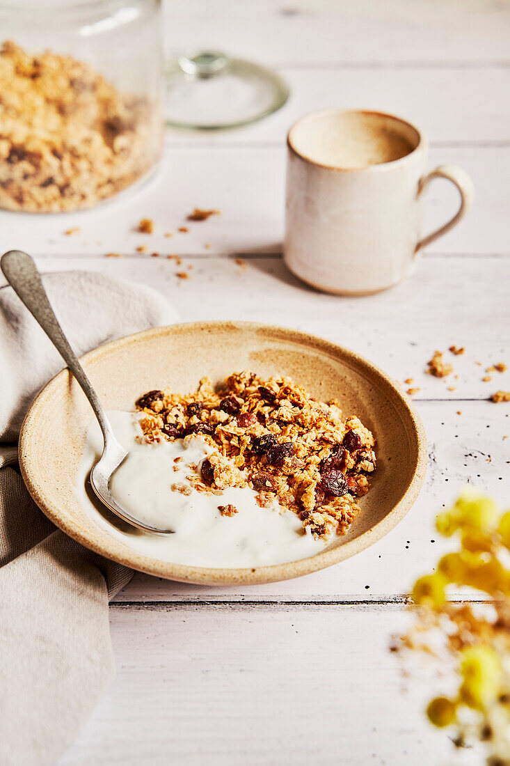 Granola mit Joghurt auf einem hellen Holztisch mit Kaffee und Serviette
