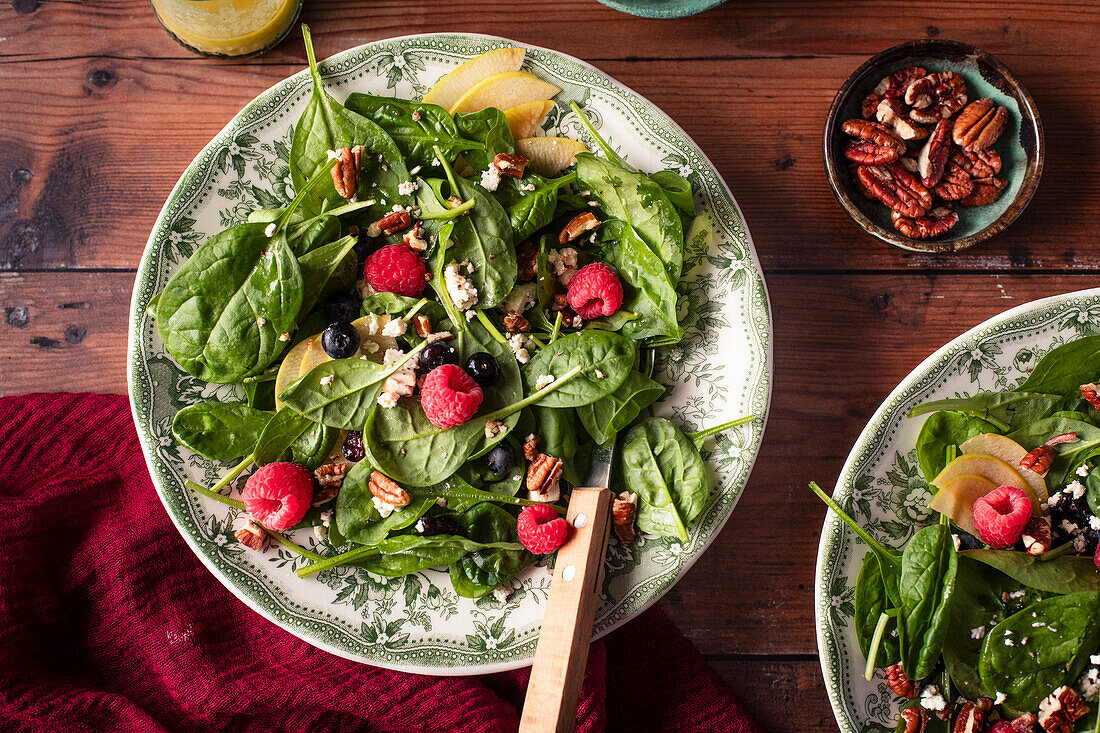 A healthy green salad with spinach and apple and raspberries in two bowls
