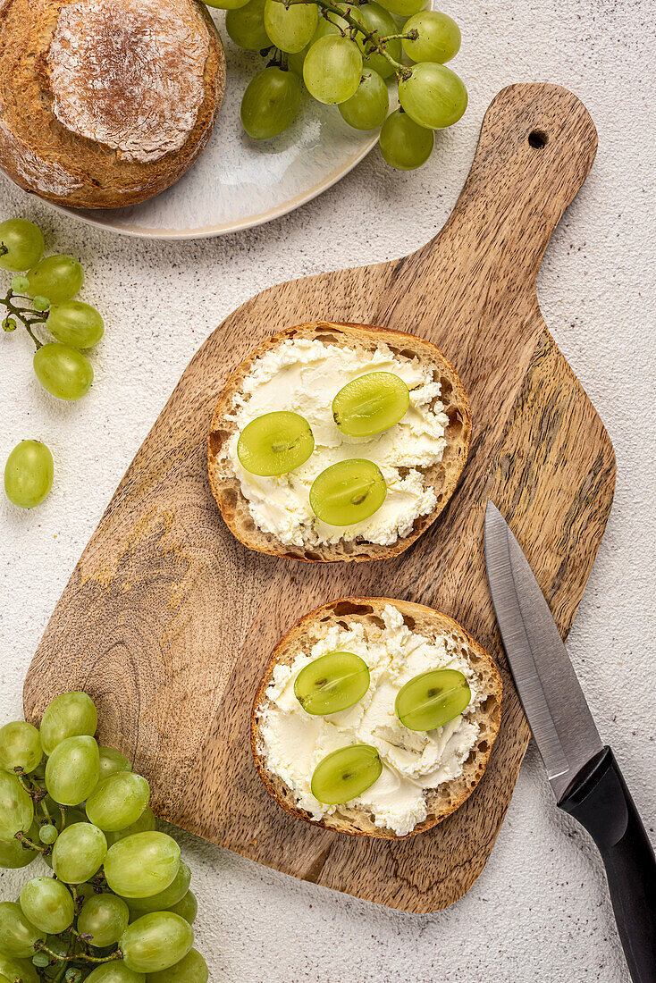 Two sandwiches with cream cheese and grapes on a chopping board