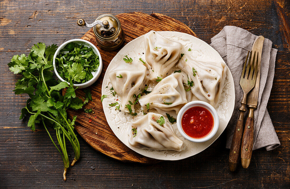 Georgische Teigtaschen Khinkali mit Fleisch, Grünzeug und würziger Tomatensauce Satsebeli auf weißem Teller