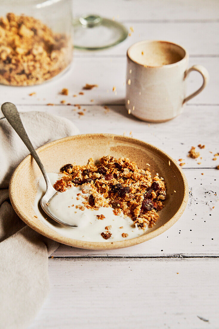 Granola with yoghurt on a light-coloured wooden table with coffee and napkin