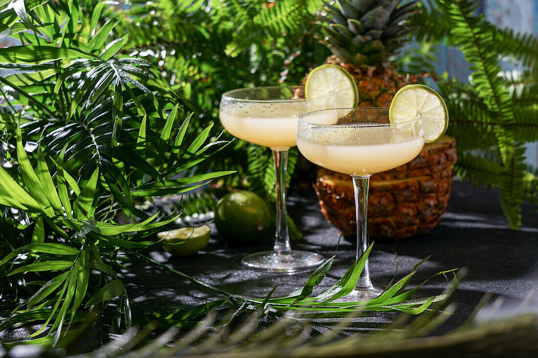 Sommercocktail Ananas-Daiquiri mit Wodka, Ananassaft, gefrorener Bewegung und fliegenden Tropfen. Tropischer Hintergrund mit Palmenblättern