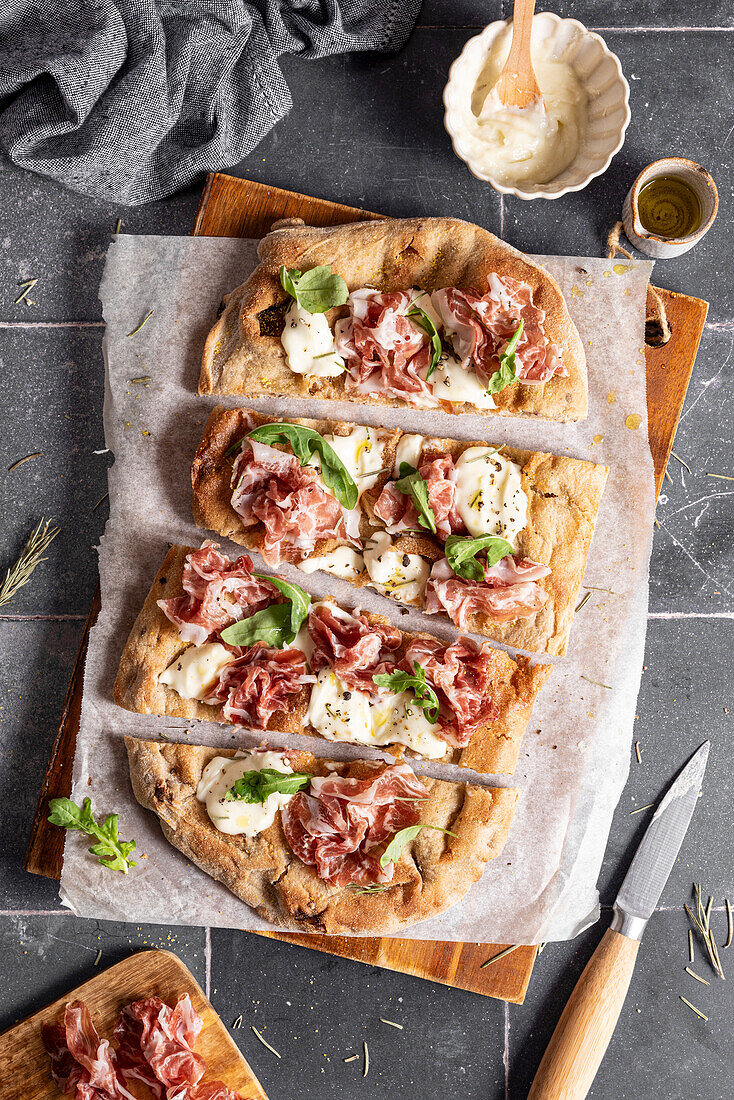 Pinsa slices with prosciutto, cheese and rocket salad