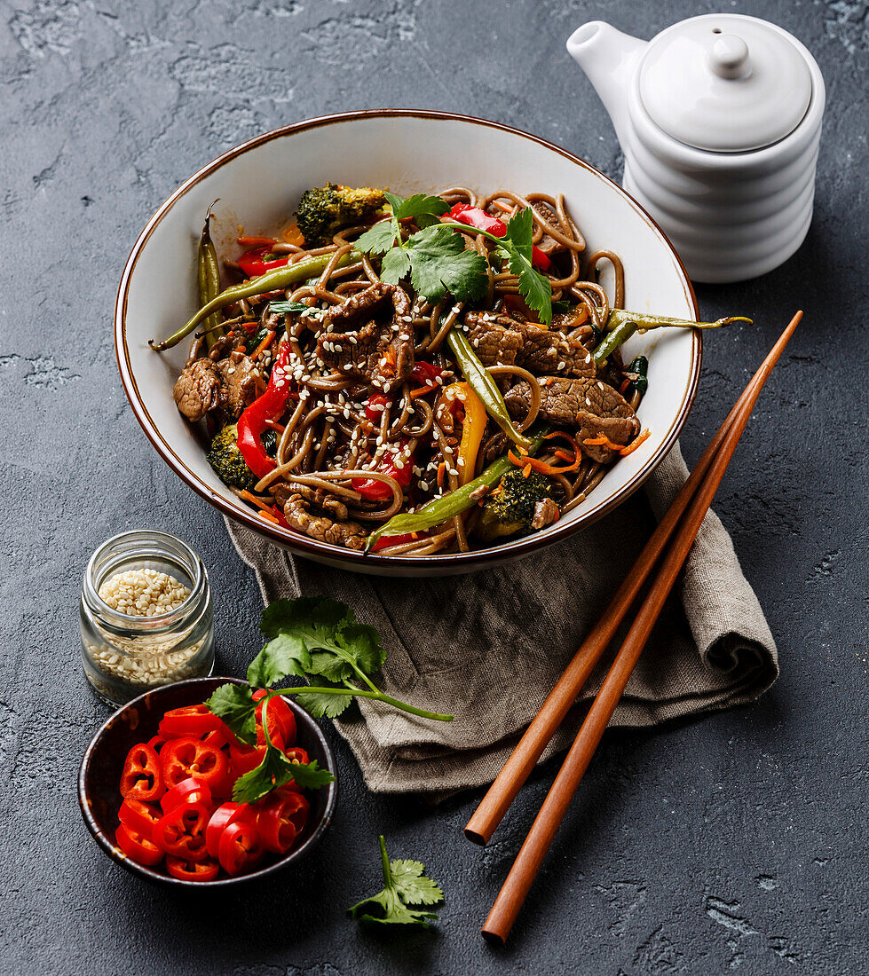 Fried soba noodles with beef and vegetables in a bowl on a dark stone background