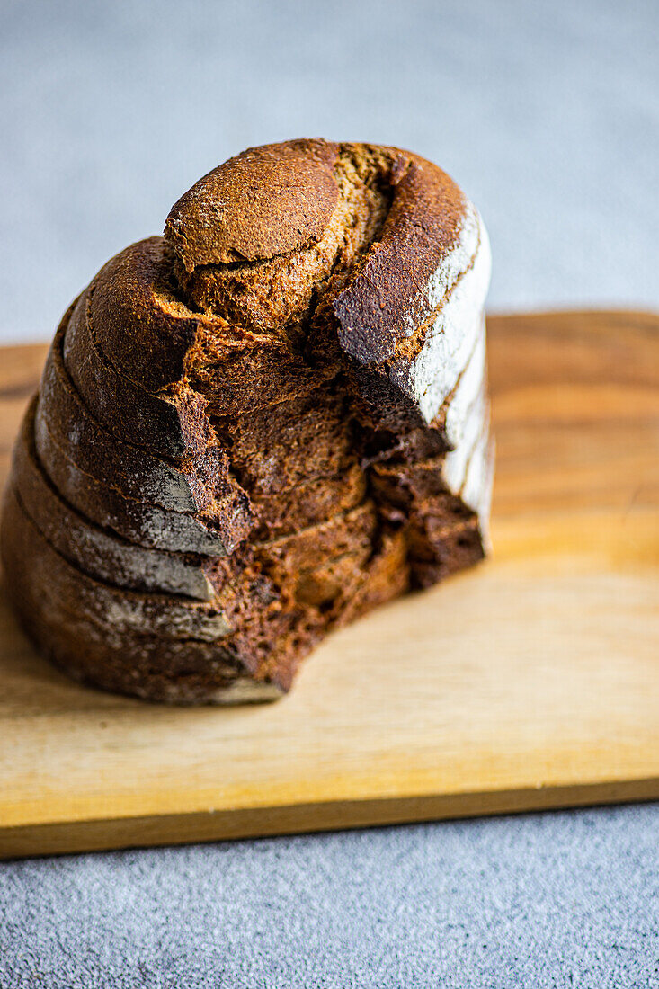 High angle of stack of rye bread slices on wooden chopping board against blurred light background