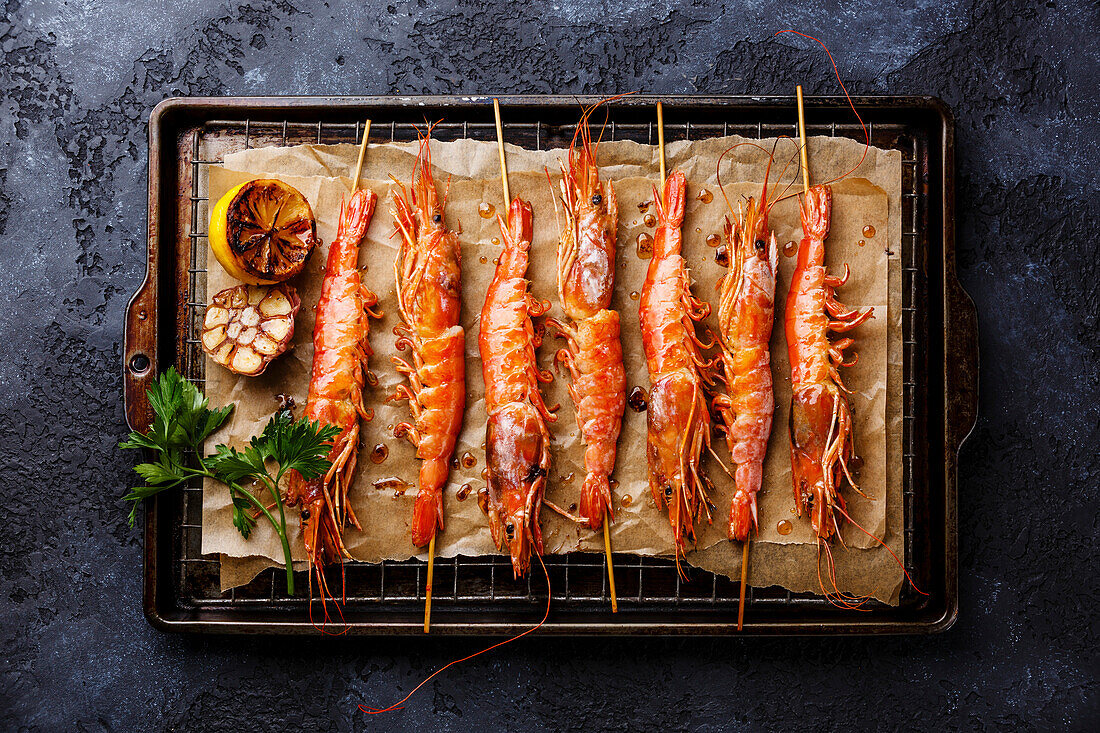 Gegrillte gebratene Garnelen Langostino Austral auf Spießchen auf Metallgitter Backblech auf schwarzem Hintergrund