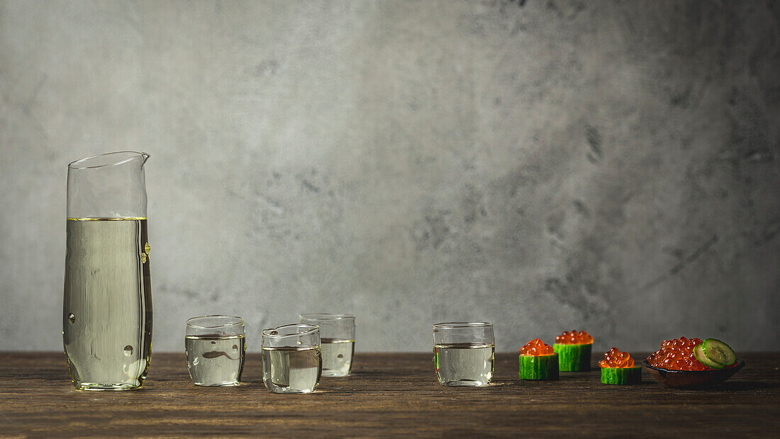 Sake in small cups and carafe with cucumber cups and salmon caviar