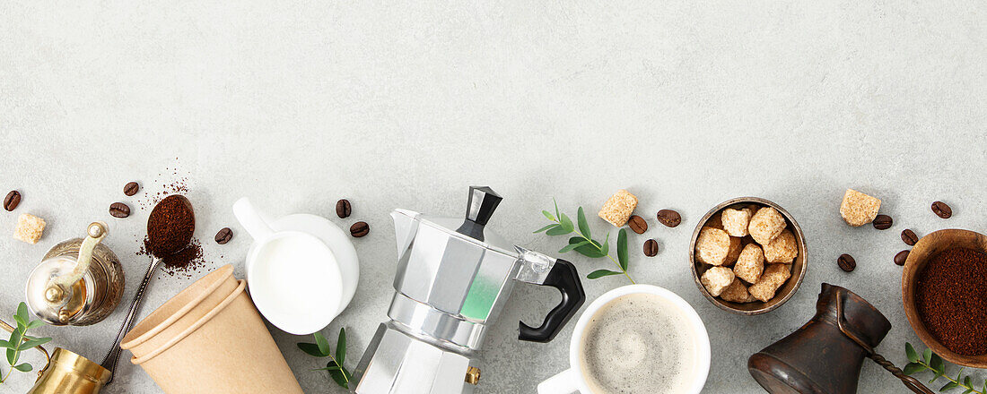 Flat lay with Moka pot, espresso cup, ground coffee, milk, sugar and coffee beans on a grey concrete background. Header with brewing coffee ingredients. Banner