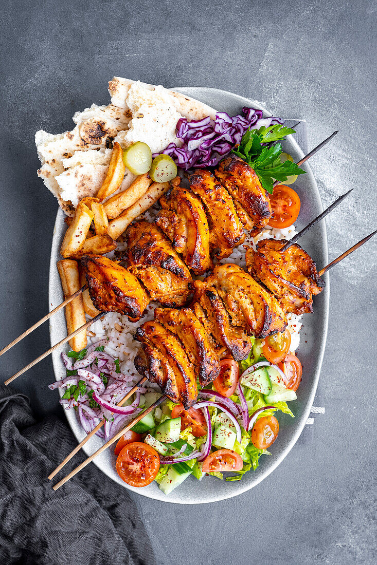 Homemade chicken kebab on a wooden skewer, served on rice, garnished with chips, pickles, salad and lavash bread on an oval plate