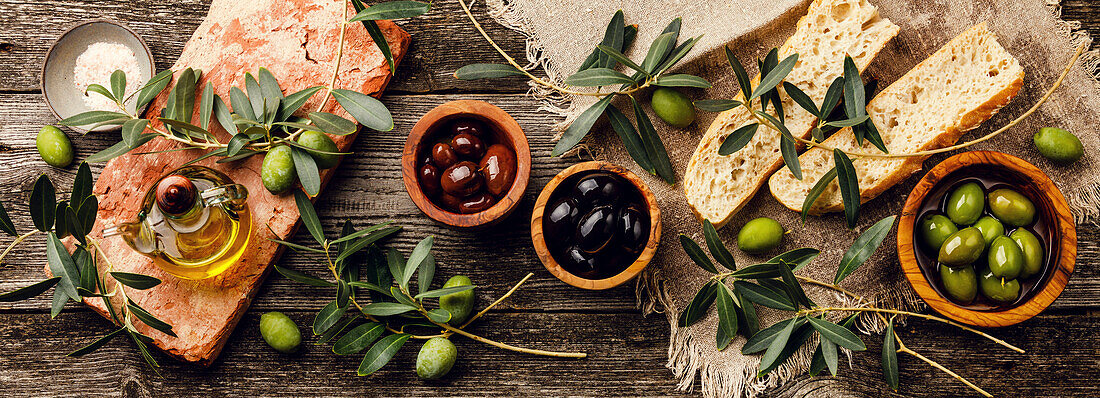 Italian food with olives, sliced ciabatta bread and olive oil on a grey wooden background