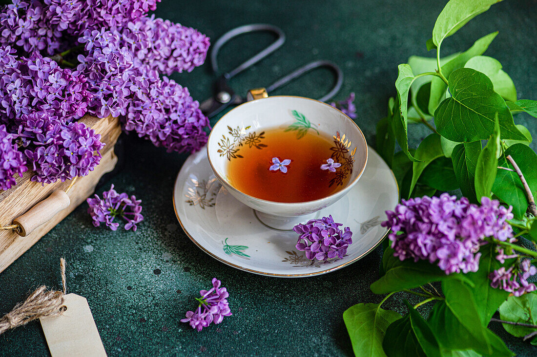 Delicious black tea in white vintage cup on mint green concrete table with aromatic lilac flowers