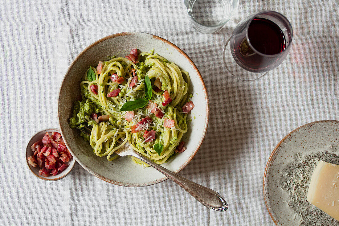 Schale mit Spaghetti mit frischem Basilikum, Pancetta, Parmesan und einem Glas Rotwein