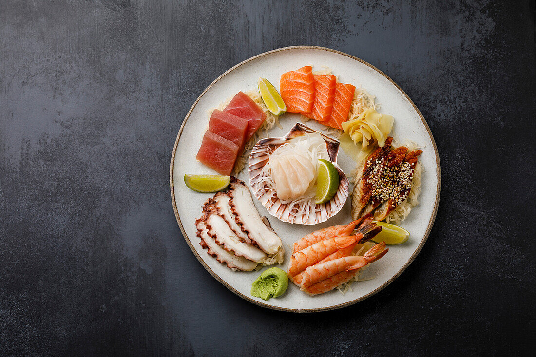 Sashimi-Sushi-Set mit Jakobsmuschel auf Muschel mit Daikon und Zitrone auf Teller auf dunklem Hintergrund