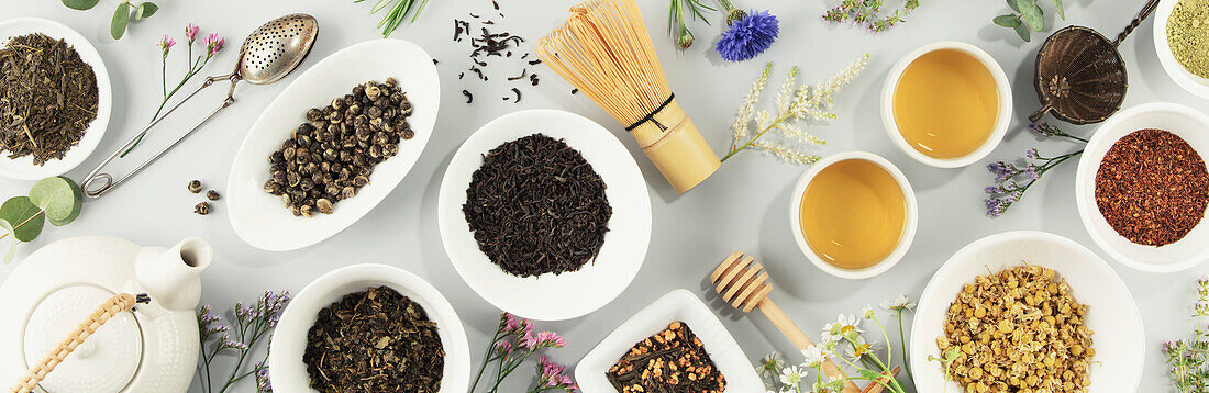 Assortment of dried teas in white ceramic bowls. Matcha, rooibos, black tea, green tea, herbal blend, masala and camomile tea. Top view, flat lay, space for menu, logo or design