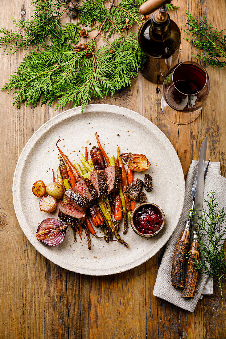 Gegrilltes Hirschsteak mit gebackenem Gemüse, Beerensauce und Rotwein auf Holzuntergrund