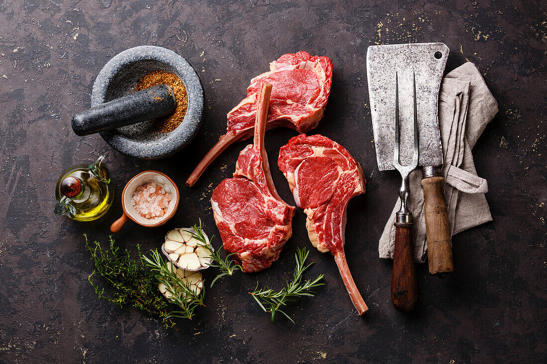 Raw fresh veal ribs with ingredients and vintage kitchen utensils on a dark background