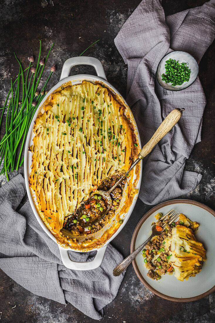 Shepherds Pie topped with mashed potatoes and chives, with serving spoon and serving on plate