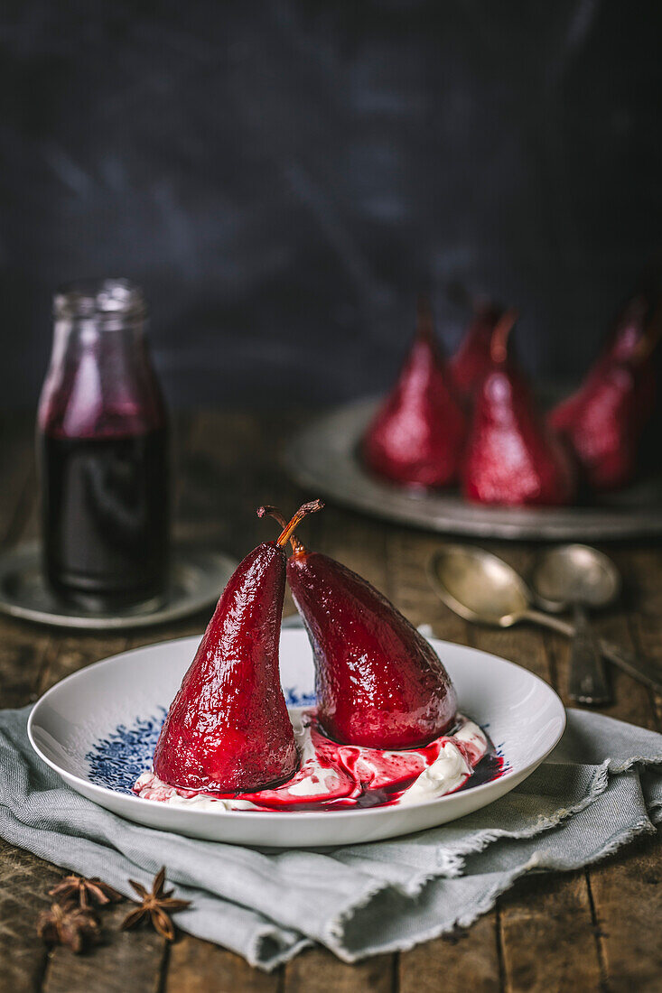 Pears poached with red wine on whipped cream, on a white and blue plate with pears in the background