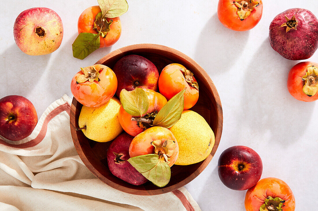 Pomegranates, persimmons, pears and apples in a bowl on a neutral background