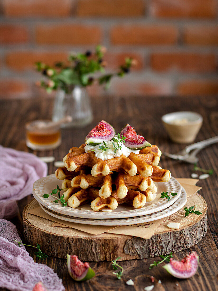 Stack of waffles with figs, cream, thyme and honey on a wooden rustic board.