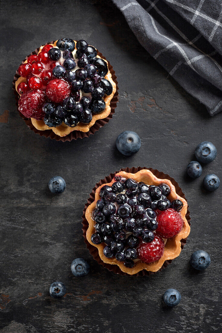 Pastry basket with blueberries and raspberries. Cake on a dark background. View from above