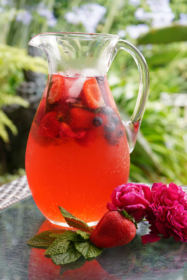 Berry and rose petal spritzer refreshing summer drink. Jug closeup in outdoor garden setting.