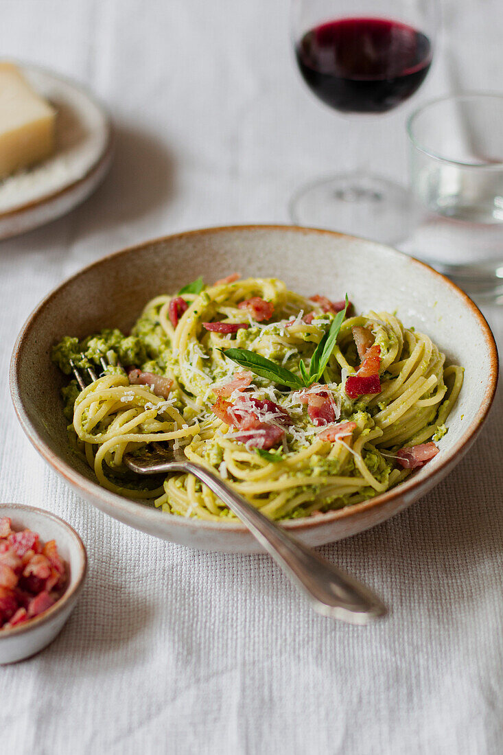 Oblique shot of a bowl of spaghetti with fresh basil, pancetta, parmesan and a glass of red wine