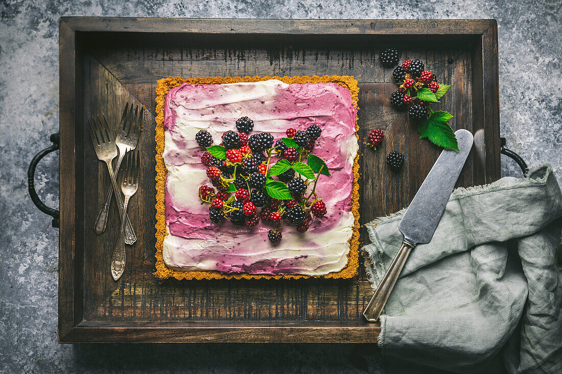 Blackberry cheesecake with berries on a wooden tray with forks and knife