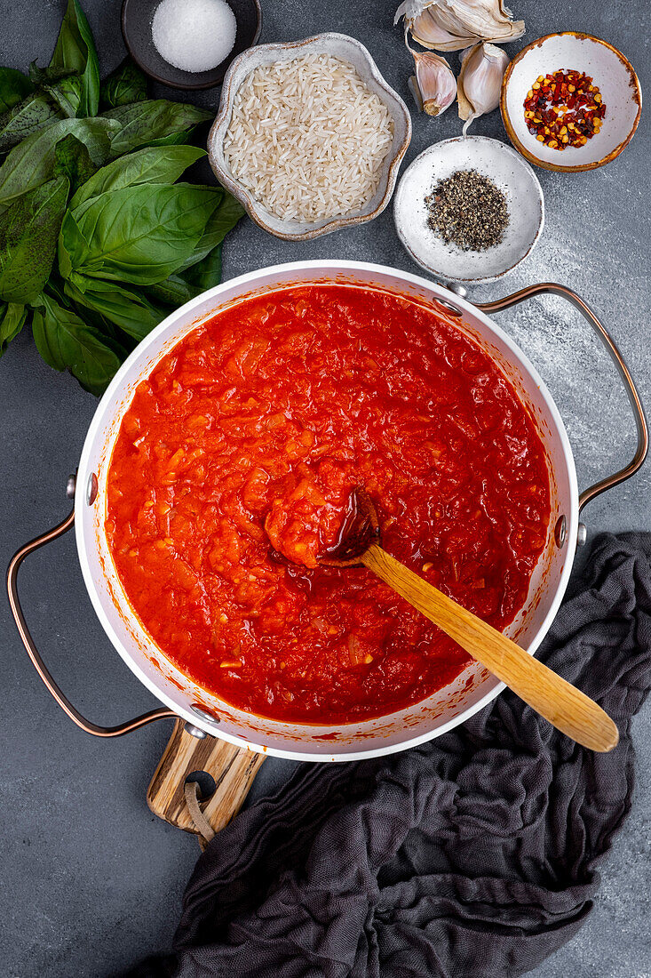 Diced onions and tomatoes are cooked in a white pot with a wooden spoon in it