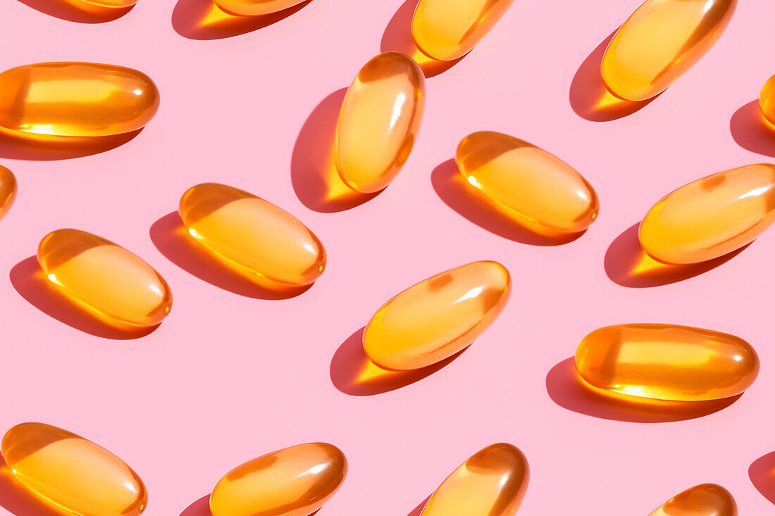Assortment of orange vitamin pills scattered on a pink background in a bright studio