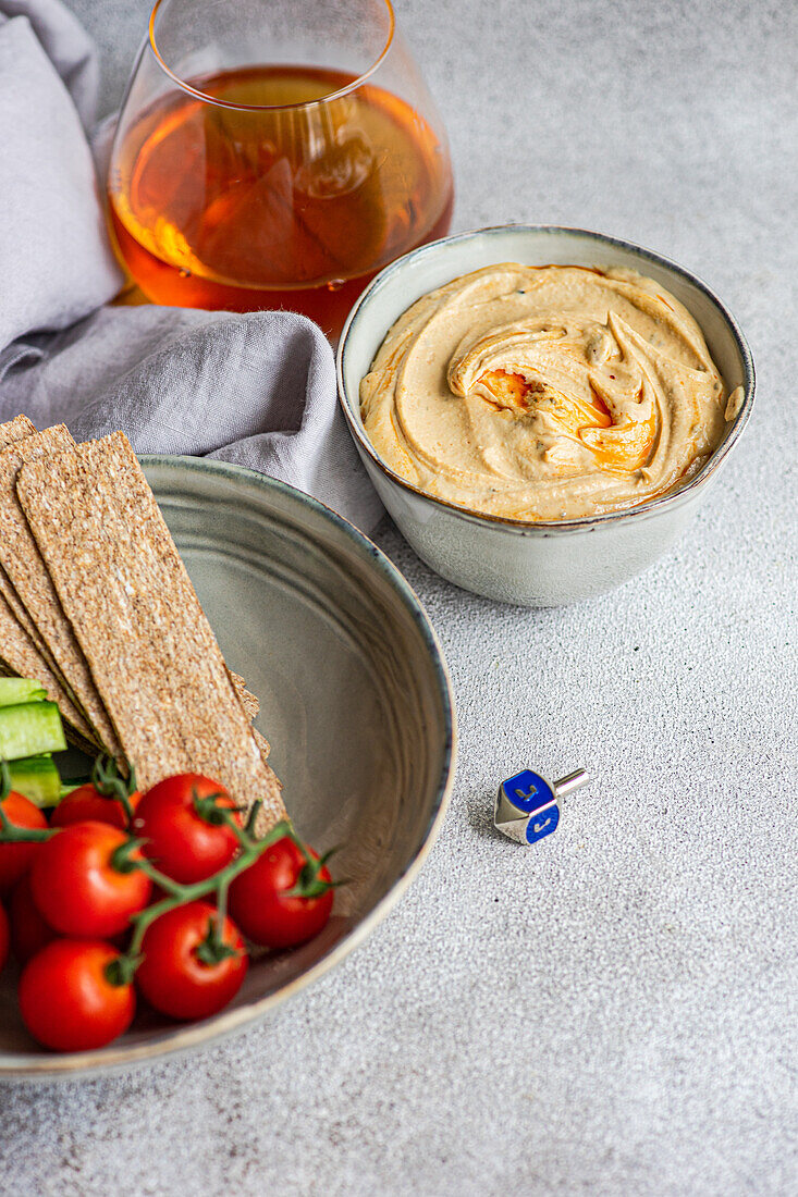 Hoher Winkel eines gesunden Pflanzentellers mit Hummus und Gemüse, serviert in Schalen neben einer Serviette und einem Glas Schnaps vor grauem Hintergrund