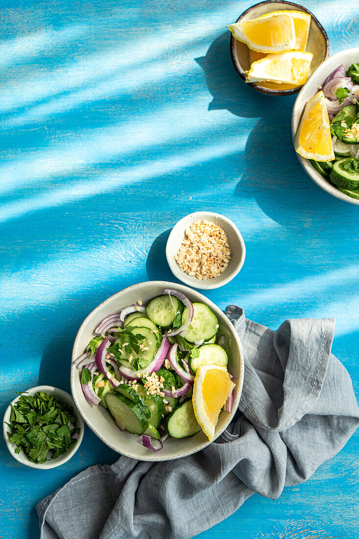 Gesunder Gemüsesalat mit Bio-Gurke, roter Zwiebel, Koriander und gehackten Nüssen auf einem blauen Betontisch von oben