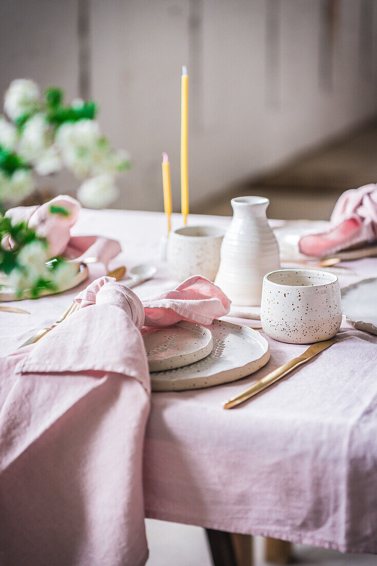 Served table with tablecloth and dishware placed near glasses for banquet in light room decorated by green potted plant