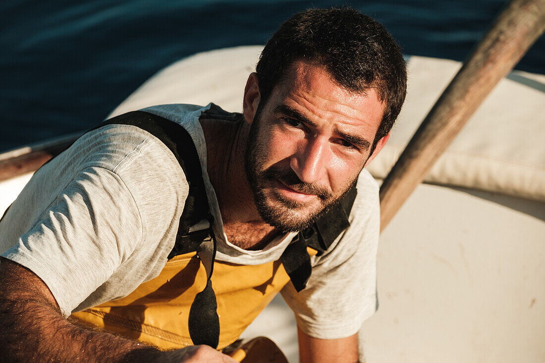 Portrait of male fisher in apron looking at camera and smiling while working on schooner in Soller on Balearic Islands in Mallorca