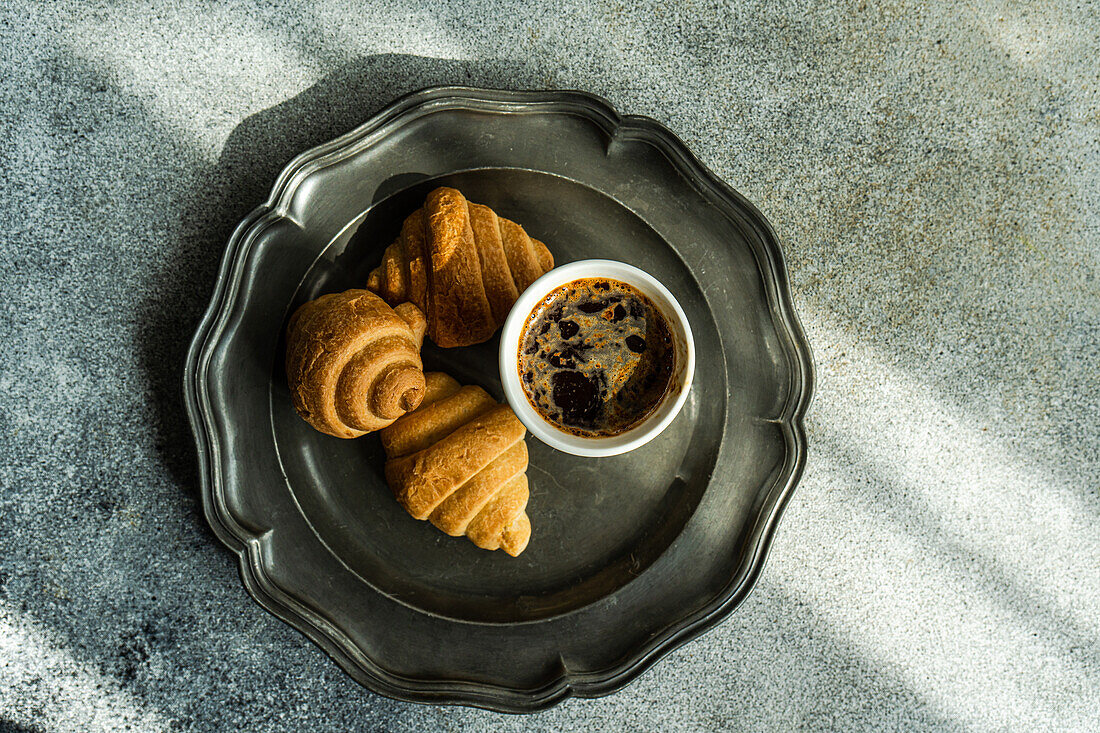 Draufsicht auf einen schwarzen Kaffee und frisch gebackene Croissants auf einem Betontisch