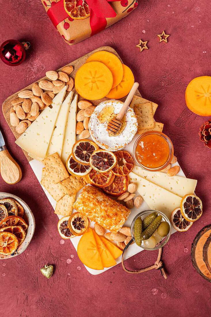 Overhead view of a gourmet cheese board with fruits, nuts, and honey, perfect for holiday entertaining, on a textured red backdrop.