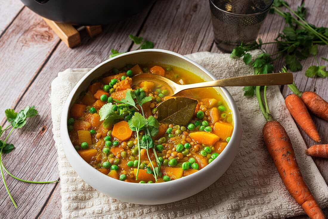 Von oben appetitliche frisch gekochte Suppe mit Karotten und grünen Erbsen, serviert in einer weißen Keramikschüssel auf einem Holztisch, dekoriert mit einem Petersilienzweig