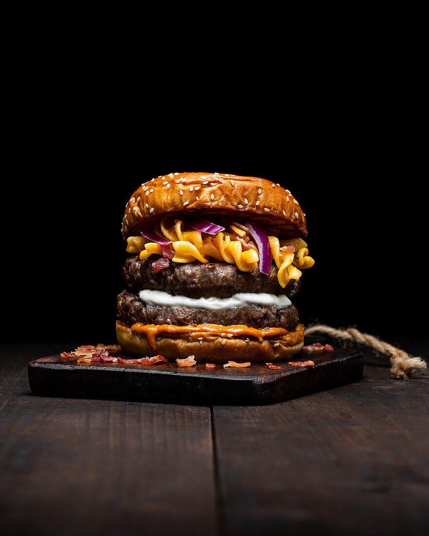 Hamburger mit Makkaroni und Käse auf einem Holztablett auf dem Tisch vor dunklem Hintergrund