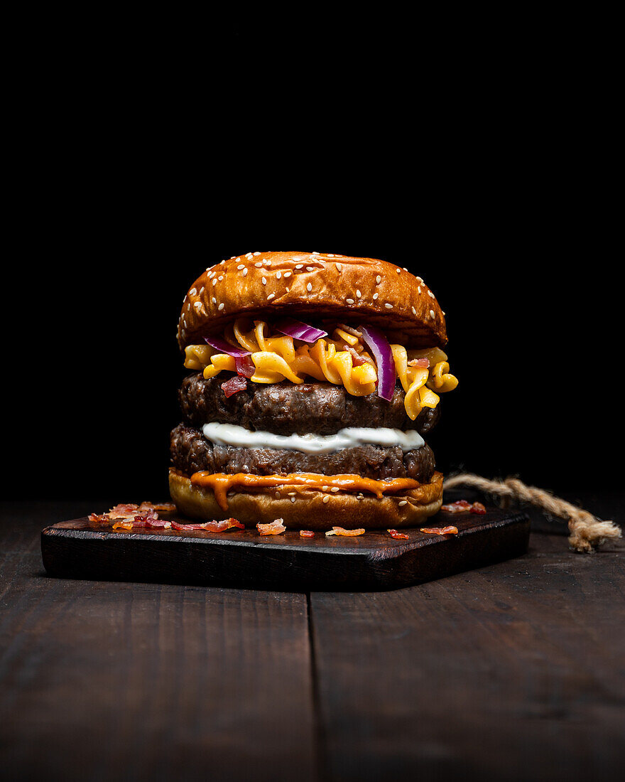 Hamburger with macaroni and cheese placed on wooden tray on table against dark background